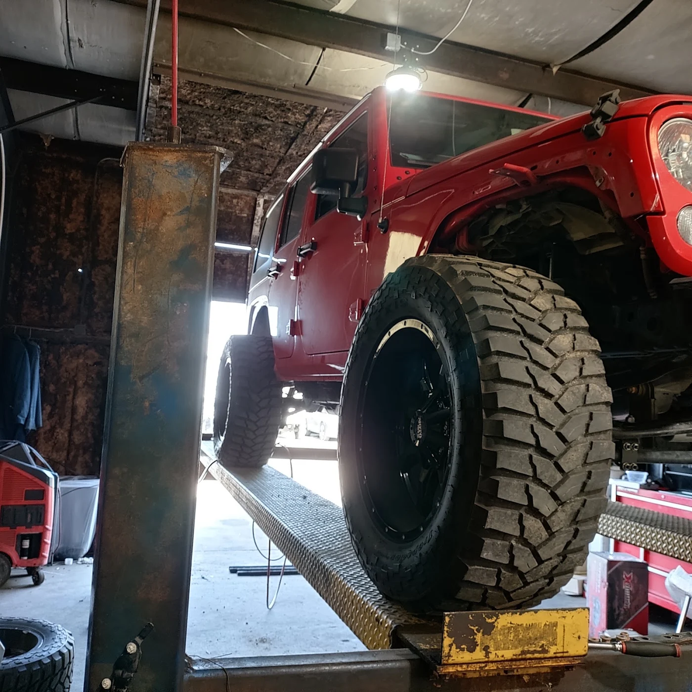 Lifted red Jeep with mud tires on the lift